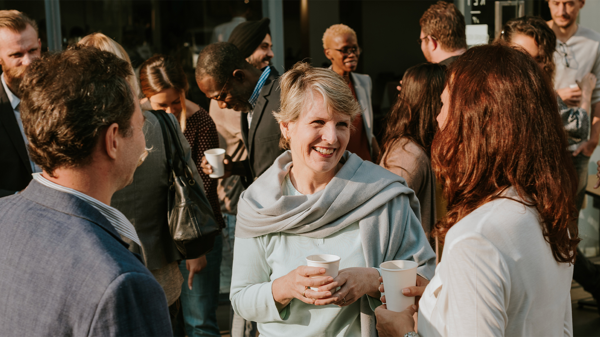 Group of diverse business people socializing outdoors, holding cups, smiling, and chatting.